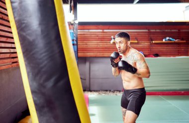 Erkek boksör kum torbasıyla yoğun bir şekilde antrenman yapıyor. Spor salonunda güç ve hassasiyet gösteriyor.
