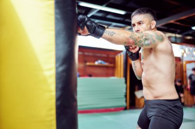 Erkek boksör ağır bir torba üzerinde yumruklarını çalışıyor. Dövüş sporlarında gereken azmi ve disiplini gösteriyor.