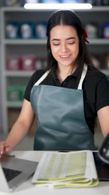 Latin Amerikalı genç bir kadın dizüstü bilgisayar kullanıyor ve küçük bir oto yedek parça şirketinde ürün listesine bakıyor.