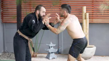 İki erkek sporcu jiu-jitsu çalışıyor, yakalama ve yer dövüşü teknikleri gösteriyor.