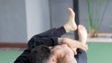 İki erkek sporcu jiu-jitsu çalışıyor, yakalama ve yer dövüşü teknikleri gösteriyor.