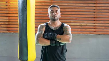 Dövmeli boksör boks eldiveni giyiyor. Spor salonunda kum torbasına karşı poz veriyor.