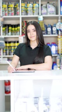 Tabletli genç Latin Amerikalı kadın küçük bir oto yedek parça dükkanının tezgahında poz veriyor.