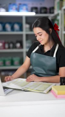 Latin Amerikalı genç bir kadın dizüstü bilgisayar kullanıyor ve küçük bir oto yedek parça şirketinde ürün listesine bakıyor.