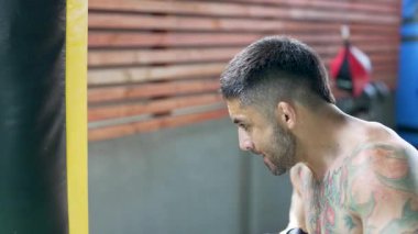 Boks eldiveni giyen erkek boksör boks salonunda kum torbasıyla antrenman yapıyor.