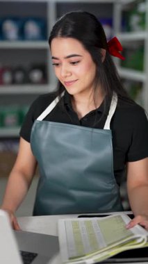 Latin Amerikalı genç bir kadın dizüstü bilgisayar kullanıyor ve küçük bir oto yedek parça şirketinde ürün listesine bakıyor.