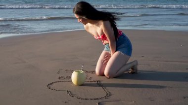 Kavun gibi içen Latin kadın bir kalp çiziyor ve kum, yaz ve tatil konseptine yazı yazıyor.