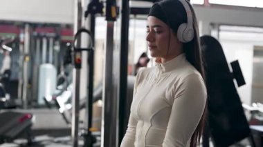 Spor salonunda halterlerle egzersiz yapan, kulaklıkla müzik dinleyen, rutin yas tutan ve sağlıklı yaşam tarzı kavramları olan Latin Amerikalı kadın.