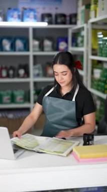 Latin Amerikalı genç bir kadın dizüstü bilgisayar kullanıyor ve küçük bir oto yedek parça şirketinde ürün listesine bakıyor.