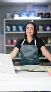 Latin Amerikalı genç bir kadın dizüstü bilgisayar kullanıyor ve küçük bir oto yedek parça şirketinde ürün listesine bakıyor.