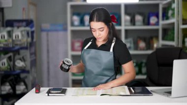 Latin Amerikalı genç bir kadın dizüstü bilgisayar kullanıyor ve küçük bir oto yedek parça şirketinde ürün listesine bakıyor.