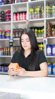 Genç Latin Amerikalı kadın küçük bir oto yedek parça dükkanında kart okuyucu tutuyor.