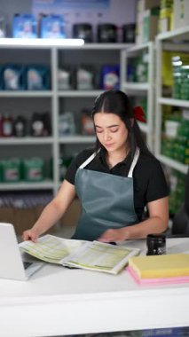 Latin Amerikalı genç bir kadın dizüstü bilgisayar kullanıyor ve küçük bir oto yedek parça şirketinde ürün listesine bakıyor.