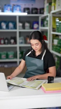 Latin Amerikalı genç bir kadın dizüstü bilgisayar kullanıyor ve küçük bir oto yedek parça şirketinde ürün listesine bakıyor.