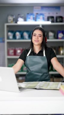 Latin Amerikalı genç bir kadın dizüstü bilgisayar kullanıyor ve küçük bir oto yedek parça şirketinde ürün listesine bakıyor.