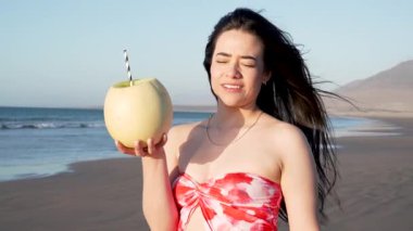 Gün batımında plajda kavun meyvesi içinde kavun içen mutlu kadın, tatil ve yaz konsepti
