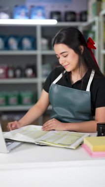 Latin Amerikalı genç bir kadın dizüstü bilgisayar kullanıyor ve küçük bir oto yedek parça şirketinde ürün listesine bakıyor.