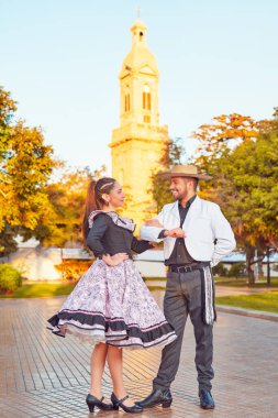 Huaso gibi giyinmiş genç bir çift birbirlerine yüz yüze bakıyor meydanda cueca dansı yapmaya hazırlar.