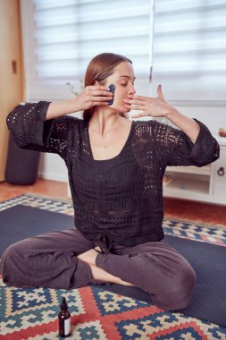 Beyaz kadın yüzüne elle masaj yapıyor. Masaj aleti, yoga ve yaşlanmayı önleyici konsept kullanıyor.