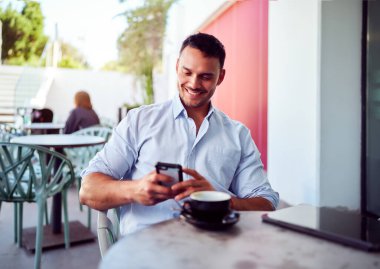 Cep telefonu kullanan ve açık kafede kahve içen mutlu girişimci.