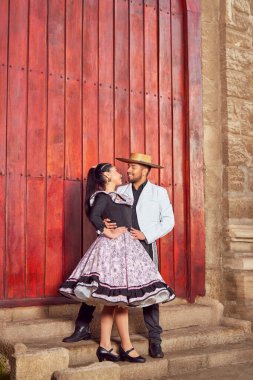 Romantik bir portre. Genç Latin Amerikalı çift yüz yüze bakıyor. Geleneksel huaso kıyafetleri içinde gülümsüyorlar.