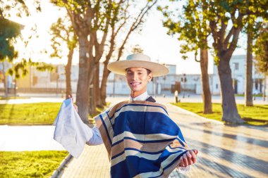Huaso kostümlü genç bir adamın portresi şehir meydanında bir mendil tutuyor.