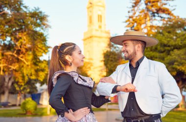 Huaso gibi giyinmiş Latin Amerikalı adam, cueca partnerini kolundan tutup dansa kaldırır.