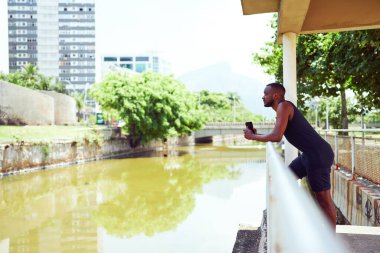 Parktaki siyah Brezilyalı bir adamın portresi. Tırabzana yaslanmış, elinde cep telefonu Ipanema 'daki manzaraya bakıyor.