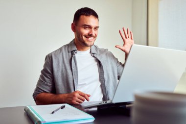 Genç girişimci, evdeki dizüstü bilgisayarla çevrimiçi toplantı sırasında meslektaşlarını selamlıyor