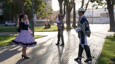 Şehir meydanında geleneksel huaso kıyafetleri içinde dans eden iki çiftin portresi.