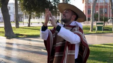 Geleneksel huaso kıyafetleri giymiş gülümseyen Latin bir adamın portresi şehir meydanındaki cueca ritmine alkış tutuyor.