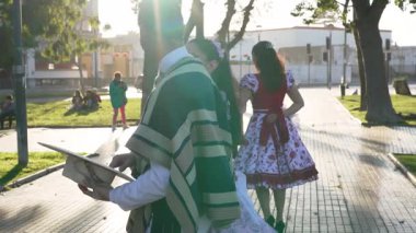 Şehir meydanında geleneksel huaso kıyafetleri içinde dans eden iki çiftin portresi.