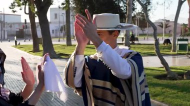 Geleneksel huaso kıyafetleri giymiş bir çiftin portresi şehir meydanındaki cueca ritmine alkış tutuyor.