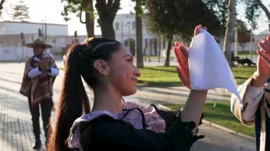 Geleneksel huaso kıyafetleri giymiş iki çiftin portresi şehir meydanındaki cueca ritmine alkış tutuyor.