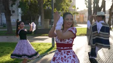 Geleneksel huaso kıyafetleri giymiş iki çiftin portresi şehir meydanındaki cueca ritmine alkış tutuyor.