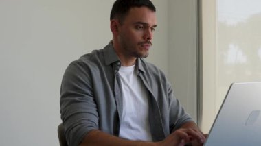 Modern bir ofiste dizüstü bilgisayarda çalışan genç bir iş adamı. 