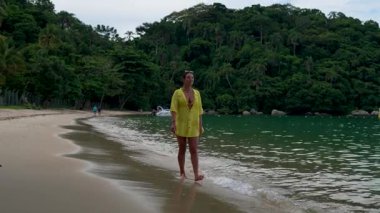 Sarı tişörtlü genç bir kadın tropikal sahilde yürüyor.
