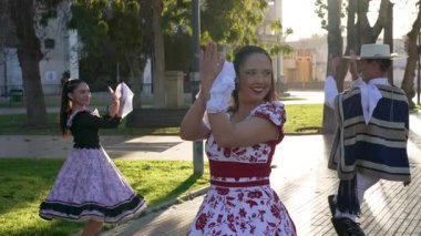 Geleneksel huaso kıyafetleri giymiş iki çiftin portresi şehir meydanındaki cueca ritmine alkış tutuyor.