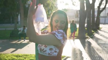 Geleneksel huaso kıyafetleri giymiş genç gülümseyen Latin kadın portresi şehir meydanındaki cueca ritmine alkış tutuyor.