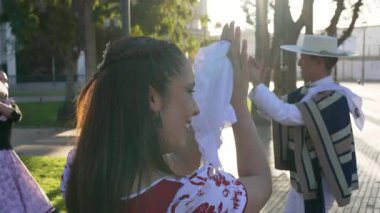 Geleneksel huaso kıyafetleri giymiş iki çiftin portresi şehir meydanındaki cueca ritmine alkış tutuyor.