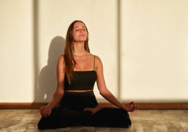 Beyaz duvar arkasında meditasyon yapan beyaz kadın portresi.