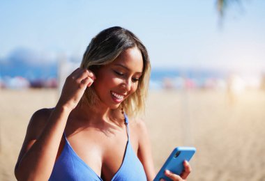 Kumsalda cep telefonuna bakıp saçını düzelten Brezilyalı genç bir kadın.