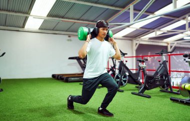 Kararlı sporcu omuzlarında ağır bir torbayla atlama egzersizi yapıyor, spor salonunda güç ve dayanıklılık kazanıyor.