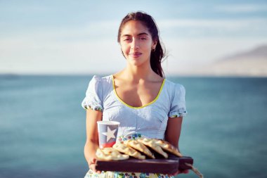 Geleneksel kostümlü Latin bir kadının portresi elinde Empanadas ve üzerinde Şili bayrağı olan geri dönüşümlü bir bardak tutuyor.