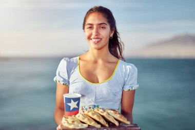 Geleneksel kostümlü Latin bir kadının portresi elinde Empanadas ve üzerinde Şili bayrağı olan geri dönüşümlü bir bardak tutuyor.