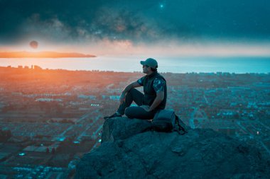 Tepenin tepesinde gün batımını seyreden bir sırt çantasının silüeti.