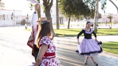 Şehir meydanında geleneksel huaso kıyafetleri içinde dans eden iki çiftin portresi.