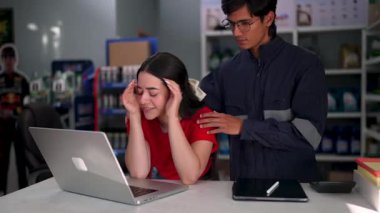 Meslektaşının yardımıyla bir mağazada dizüstü bilgisayar kullanırken çeşitli duygular edinen satış elemanı.