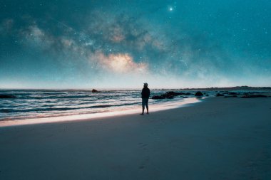 Sahilin kıyısında durmuş Pasifik Okyanusu 'nun üzerindeki yıldızlı gökyüzüne bakan bir adamın silueti.