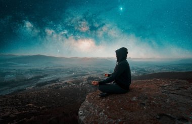 Dağın tepesinde oturmuş dışarıda meditasyon yapan biri.